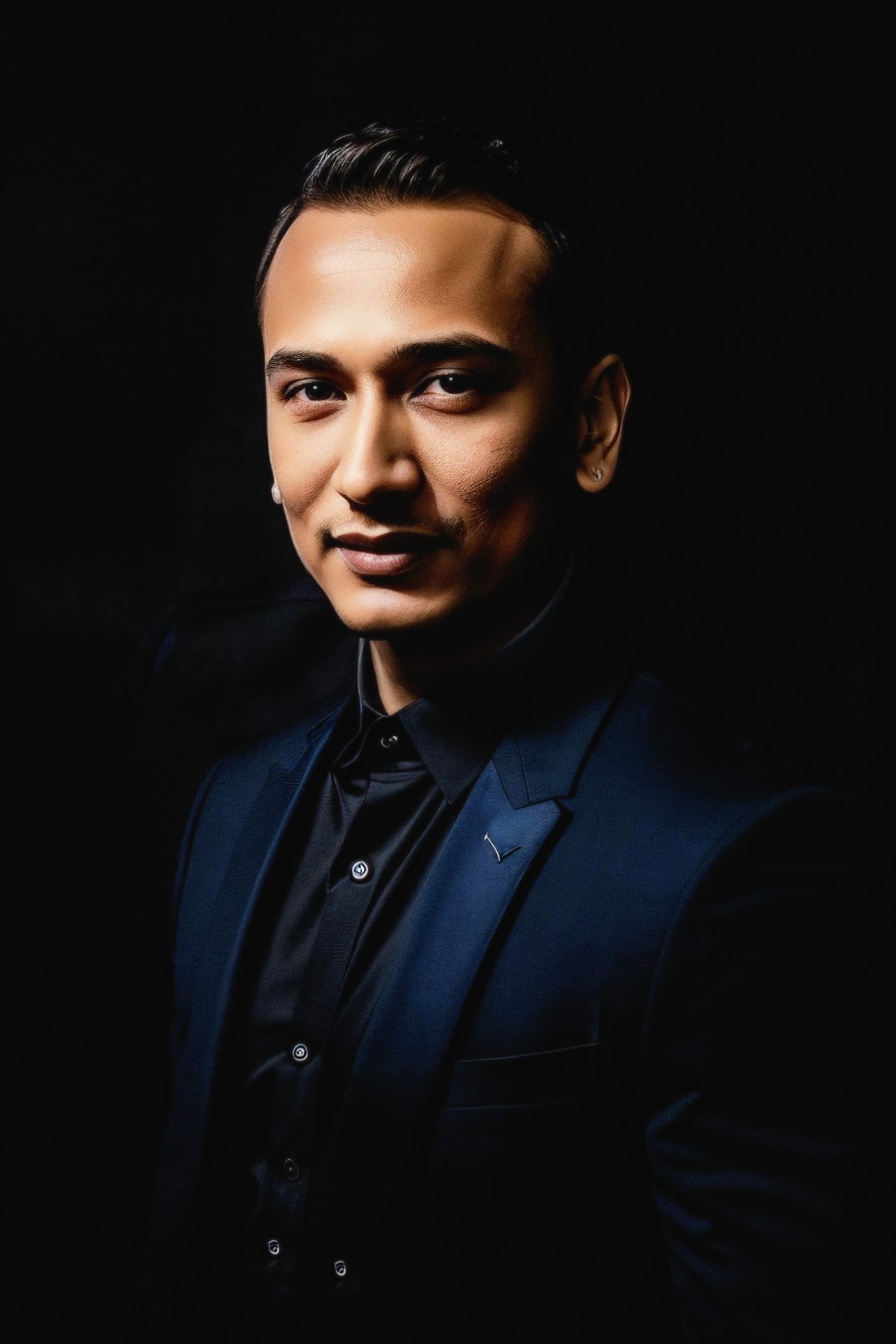 Snehaashish Pathakk in a navy suit and black shirt, photographed against a black background.